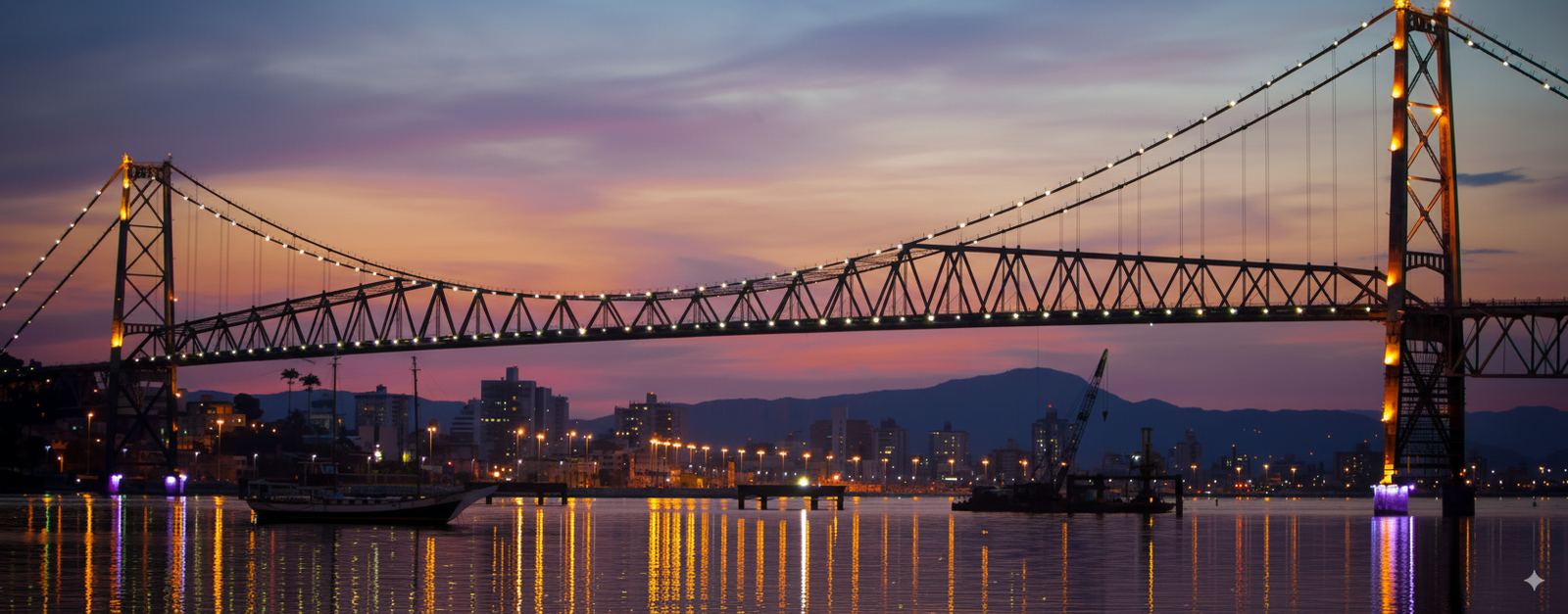 Ponte Hercílio Luz iluminada ao entardecer, vista da baía de Florianópolis